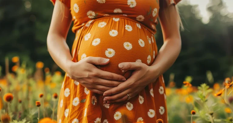 A pregnant woman in an orange dress stands in a colorful field of flowers