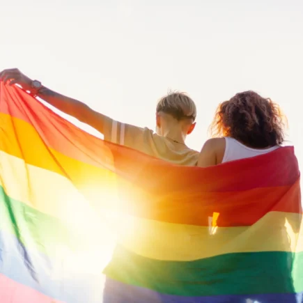 A beautiful young couple gently lovingly embraces and holds a rainbow flag