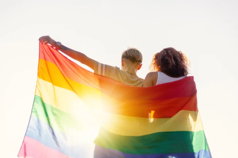 A beautiful young couple gently lovingly embraces and holds a rainbow flag