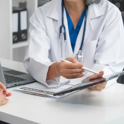 A doctor is talking to a younger woman across a desk in a medical office