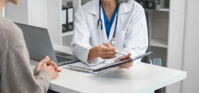 A doctor is talking to a younger woman across a desk in a medical office