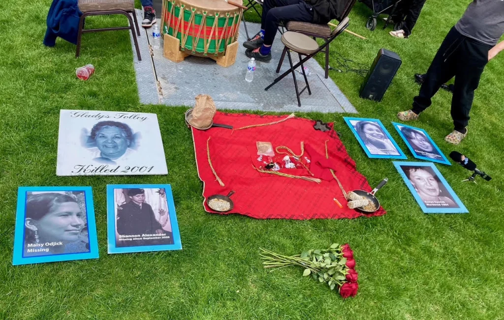 Photo of items laid out on the grass including photos of various Missing and Murdered Indigenous women, roses laid in their memory, and a ceremonial drum.
